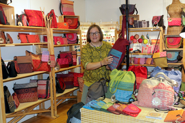 Frau mit bunten Taschen in einem Geschäft, umgeben von Regalen voller Handtaschen.