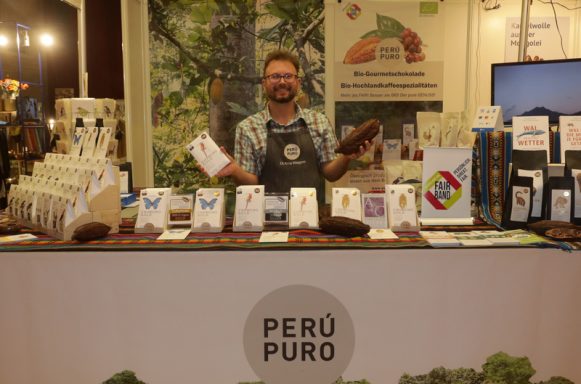Mann steht an einem Verkaufsstand mit Produkten aus Peru und lächelt freundlich.
